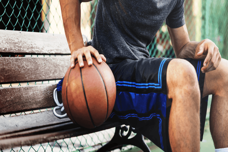 basketball player sitting on bench holding hand on ball