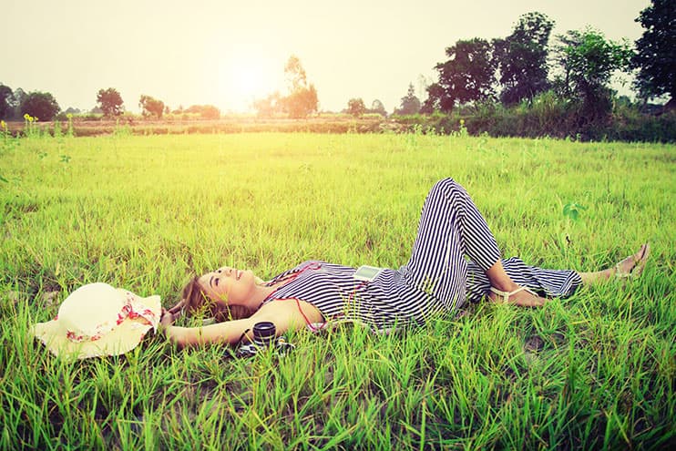 Smiling Woman Laying Down In The Grass Under A Shiny Sun